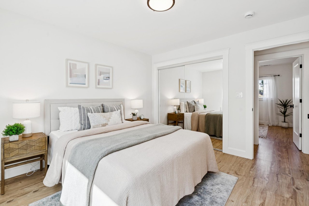Staged bedroom with a large neutral-toned bed, matching nightstands, and light wood flooring.