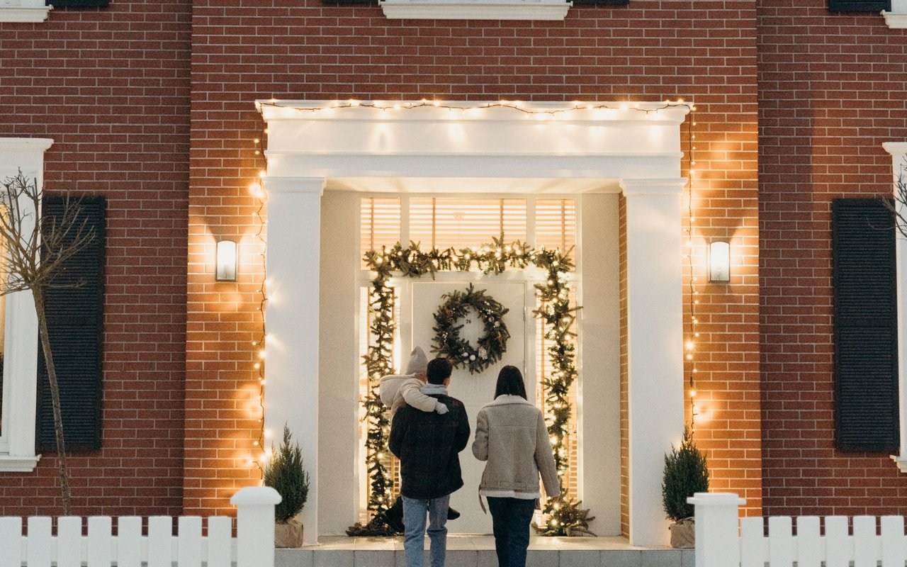 Family entering a red-brick home through a warmly lit, holiday-decorated entrance.