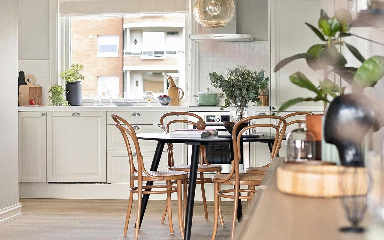 Bright kitchen with cream cabinets, a large window, and a black dining table with wooden chairs.
