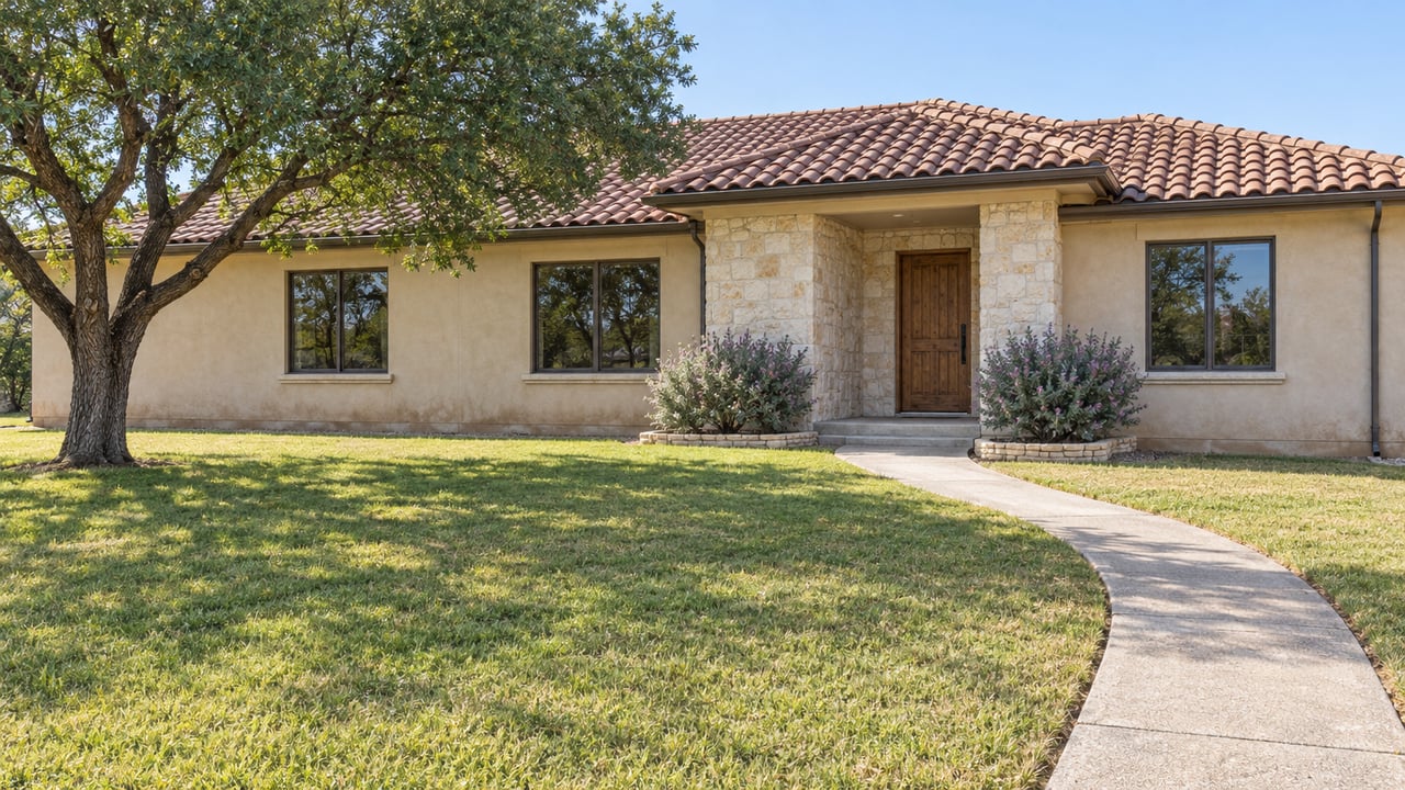 Single-story sand-stucco home with a terracotta roof, limestone entry, deep front lawn and a mature shade tree.