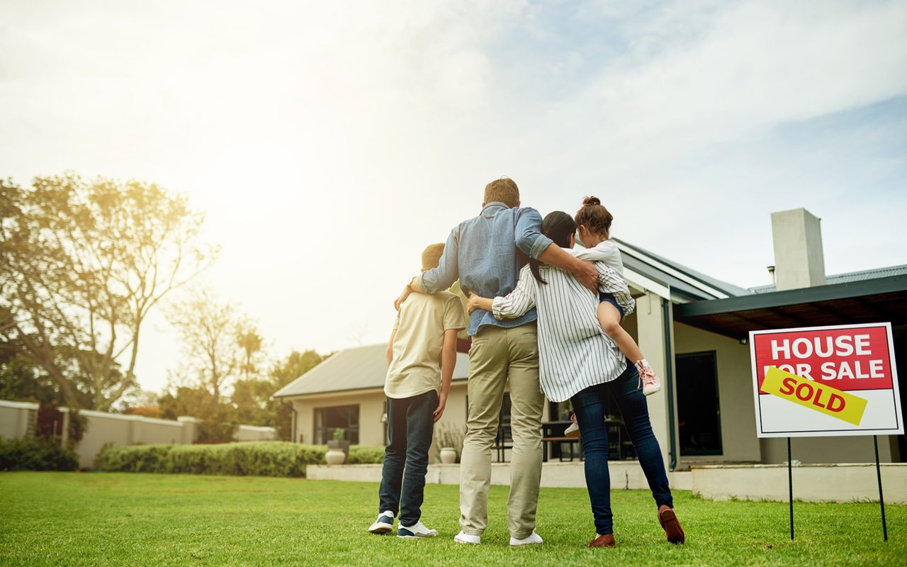 Family embraces on a lawn outside their newly sold modern home.