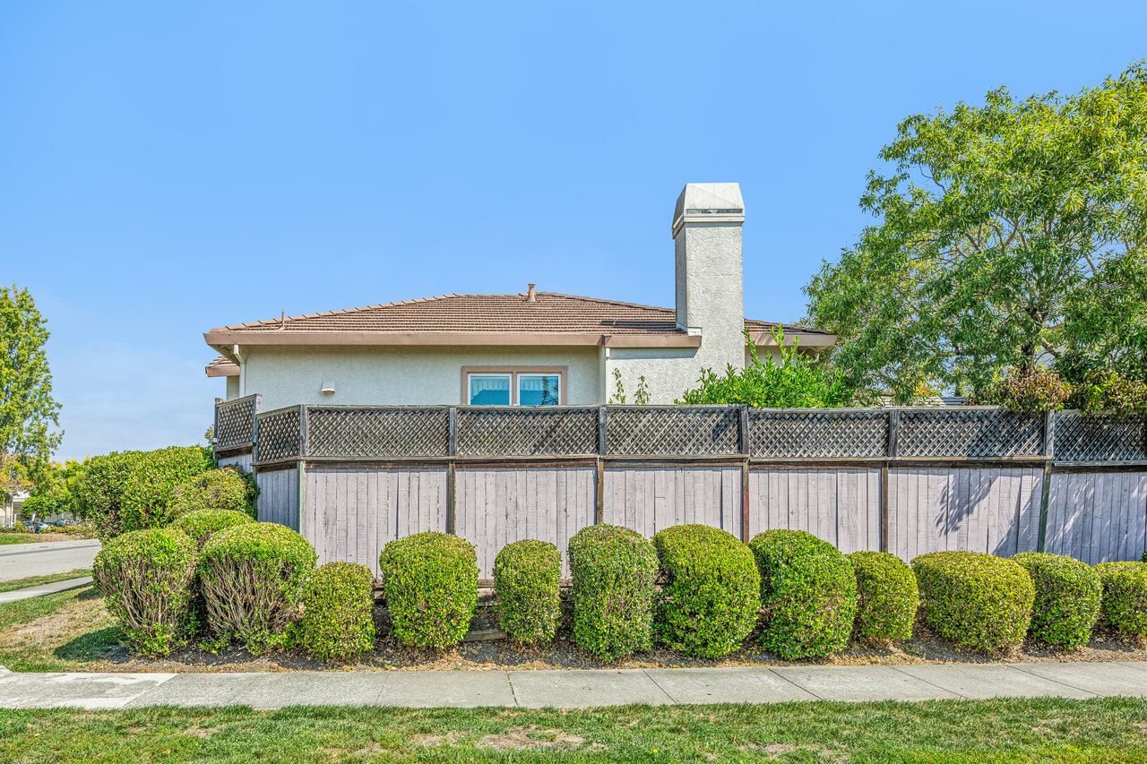 House exterior behind a tall lattice fence and neatly trimmed hedges.