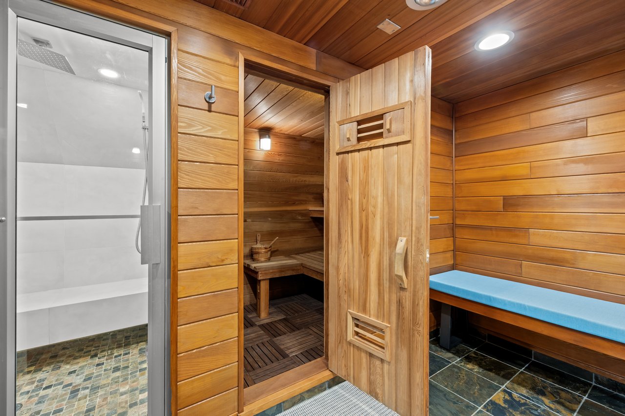 Home sauna with wood-paneled walls, built-in benches, and an adjacent glass-enclosed shower.