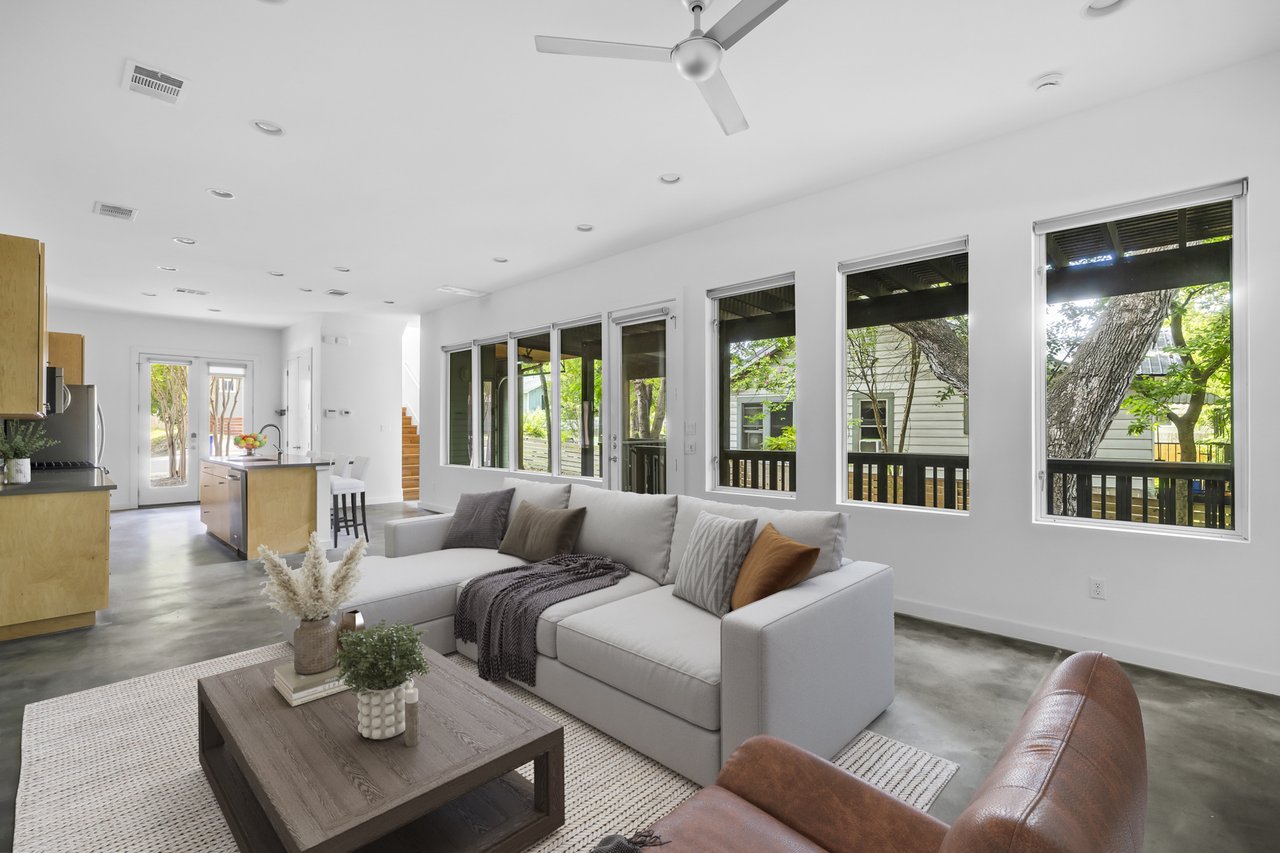 Living room at 1302 S 5th St Unit A, Bouldin, Austin, TX, with a gray sectional, concrete floors, and a wall of windows framing a treed view.