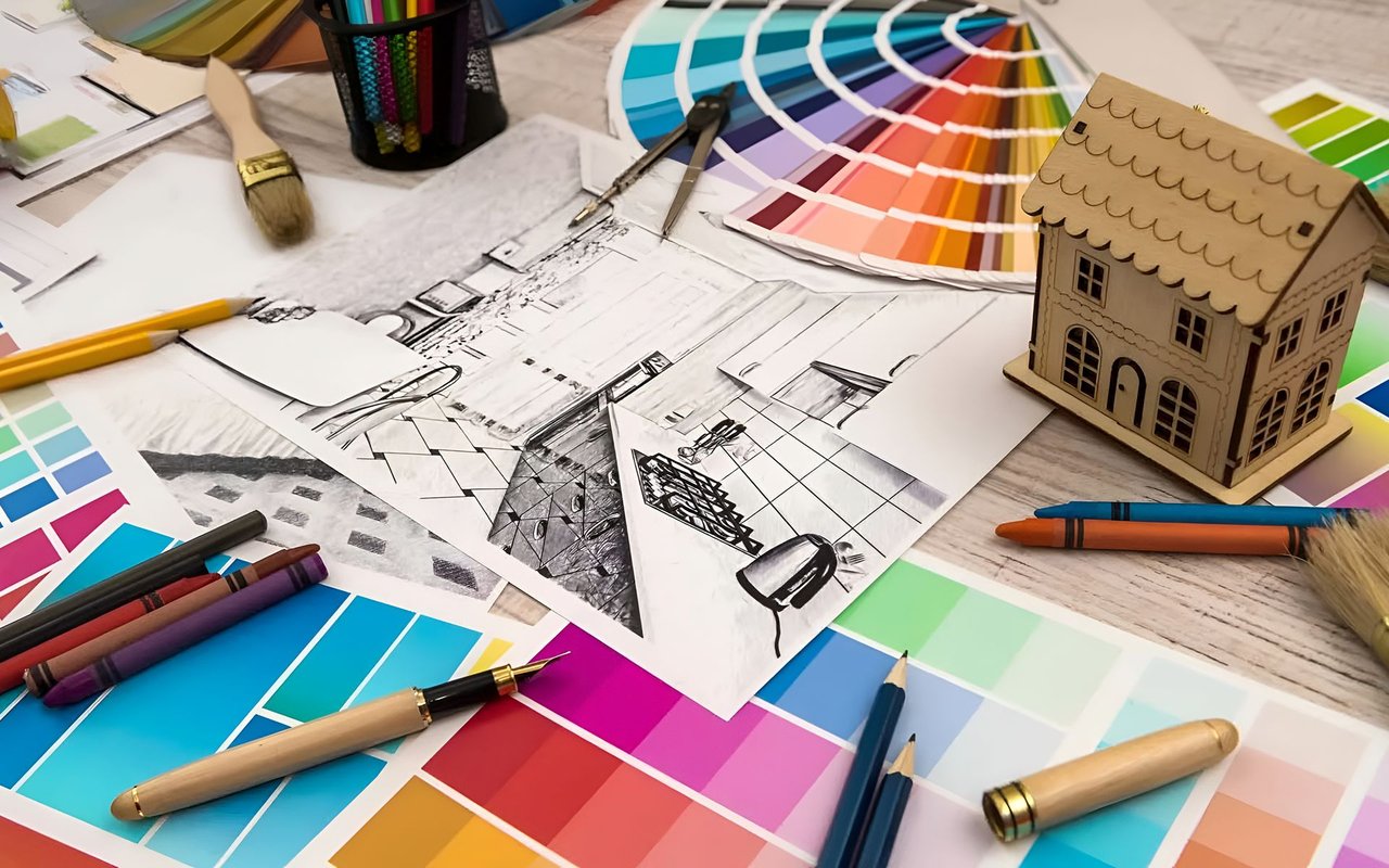 Model house on architectural plans surrounded by colorful paint swatches and design tools