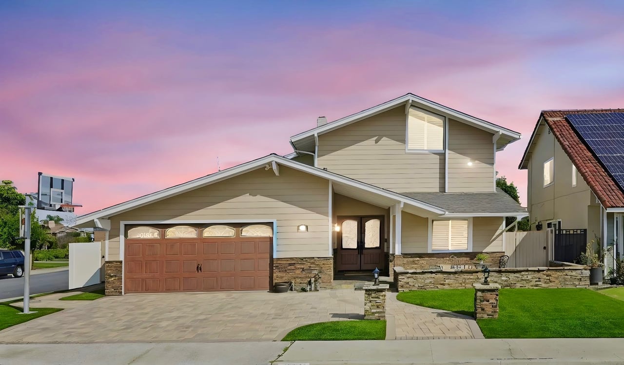Two-story beige home with a brown double garage, stone accents, and landscaped lawn at dusk.