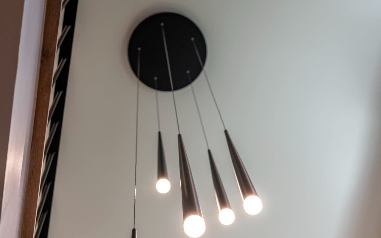 Four slim pendant lights hang beside curved wood trim.