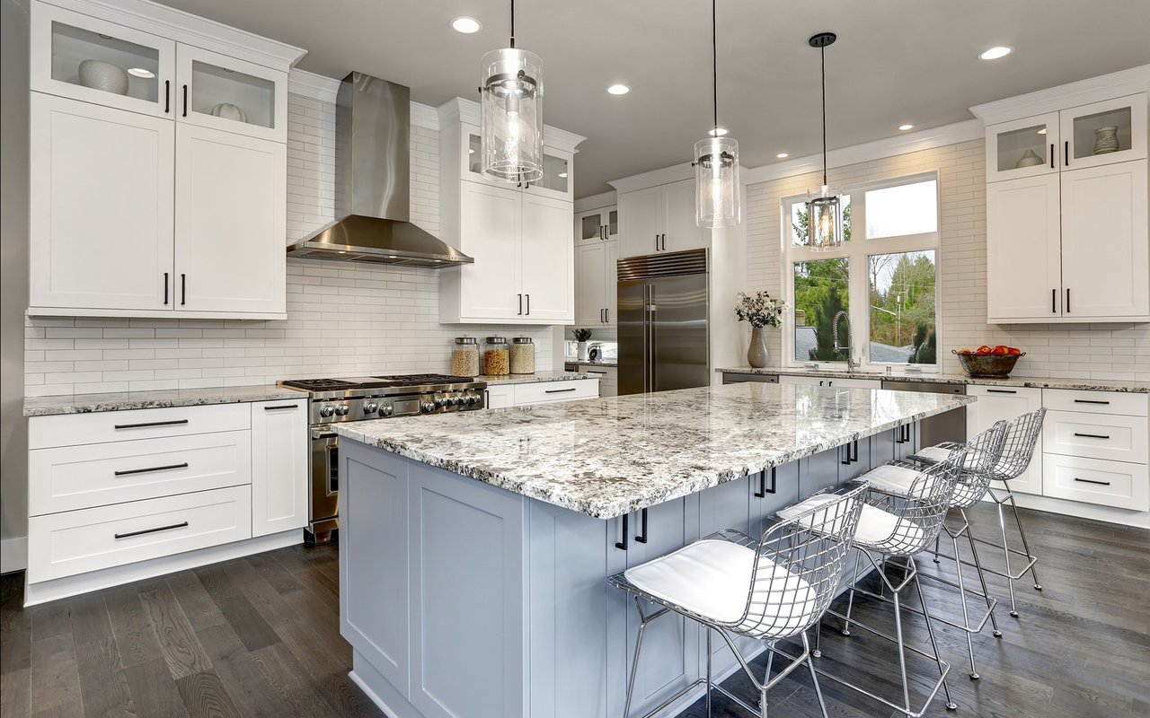 Bright kitchen with white cabinetry, a large blue island, veined stone counters, and metal bar stools.