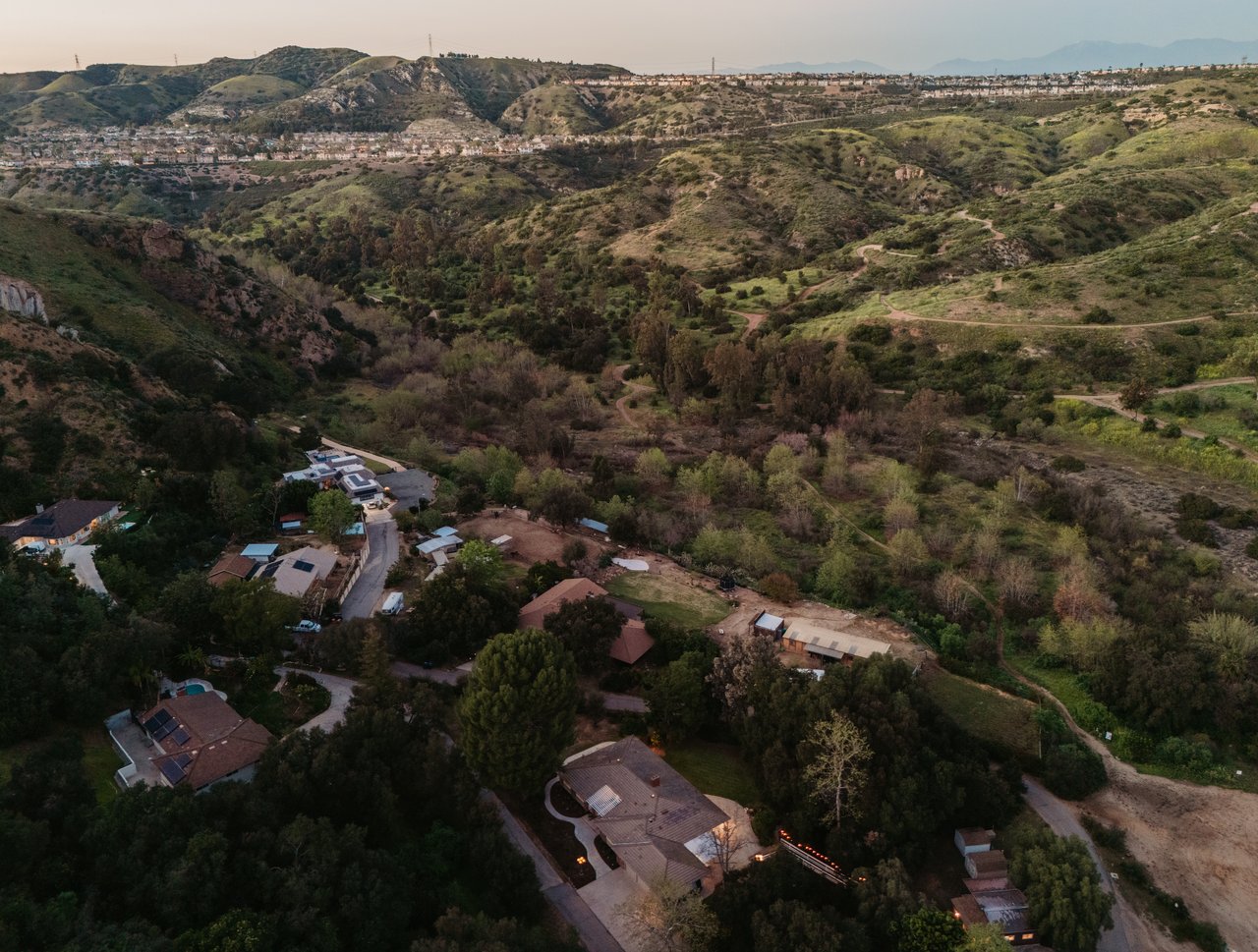 Aerial view of homes among wooded hills, winding roads, and open green space.