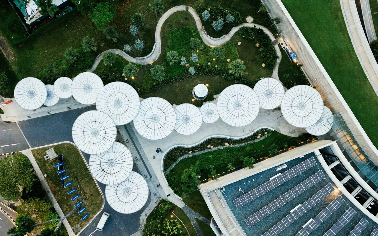 Commercial building with rooftop solar panels beside a landscaped courtyard and circular white canopies.