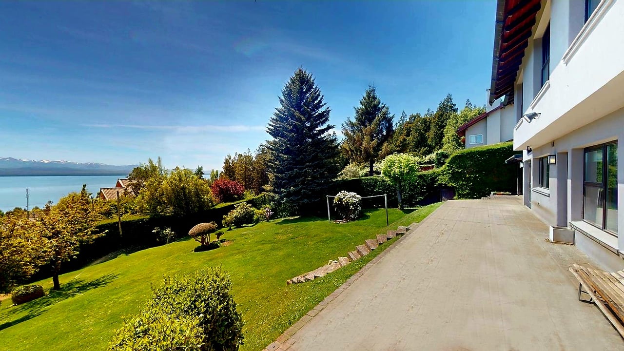 House terrace overlooking a landscaped lawn, lake, and distant mountains.