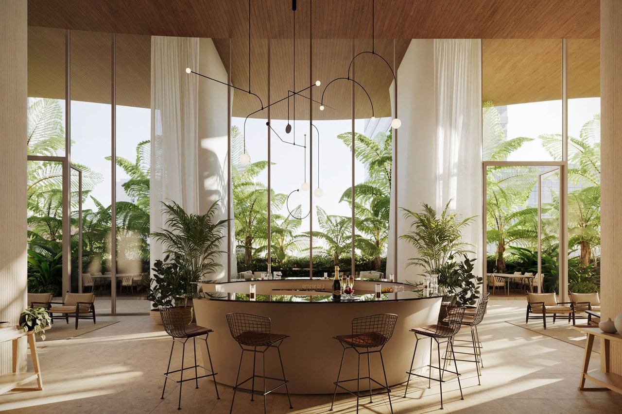Bright communal interior with a central island, sculptural pendant lights, and tropical plants beside tall windows.
