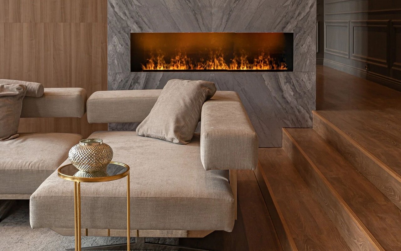 A modern living room featuring a long, horizontal fireplace set into a gray marble wall, with a beige sofa nearby.