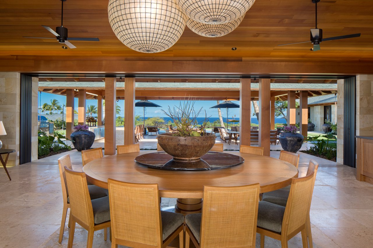 Open-air dining area with a round wooden table and ocean views.