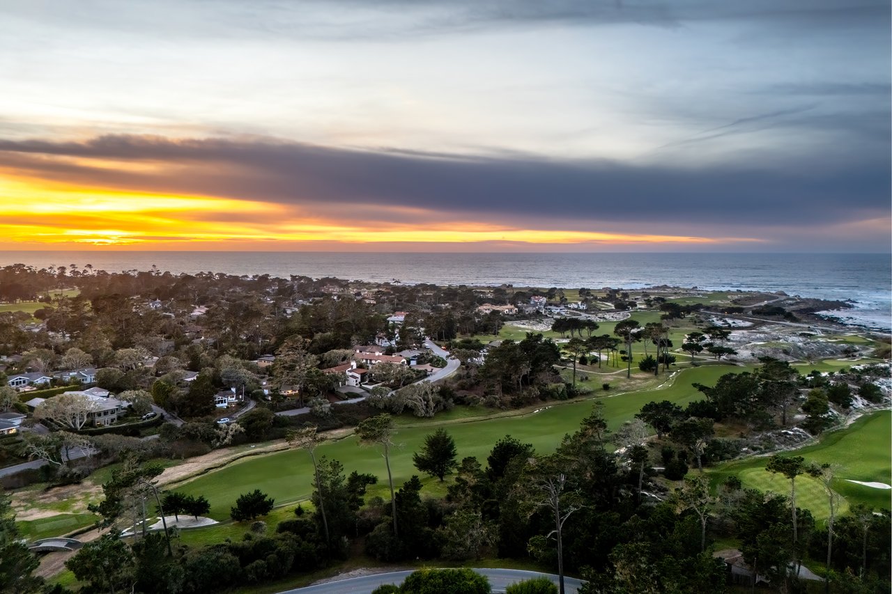 Aerial sunset view of Pebble Beach Golf Links fairways, sand bunkers, and coastal homes along the Pacific Ocean in Monterey County, California