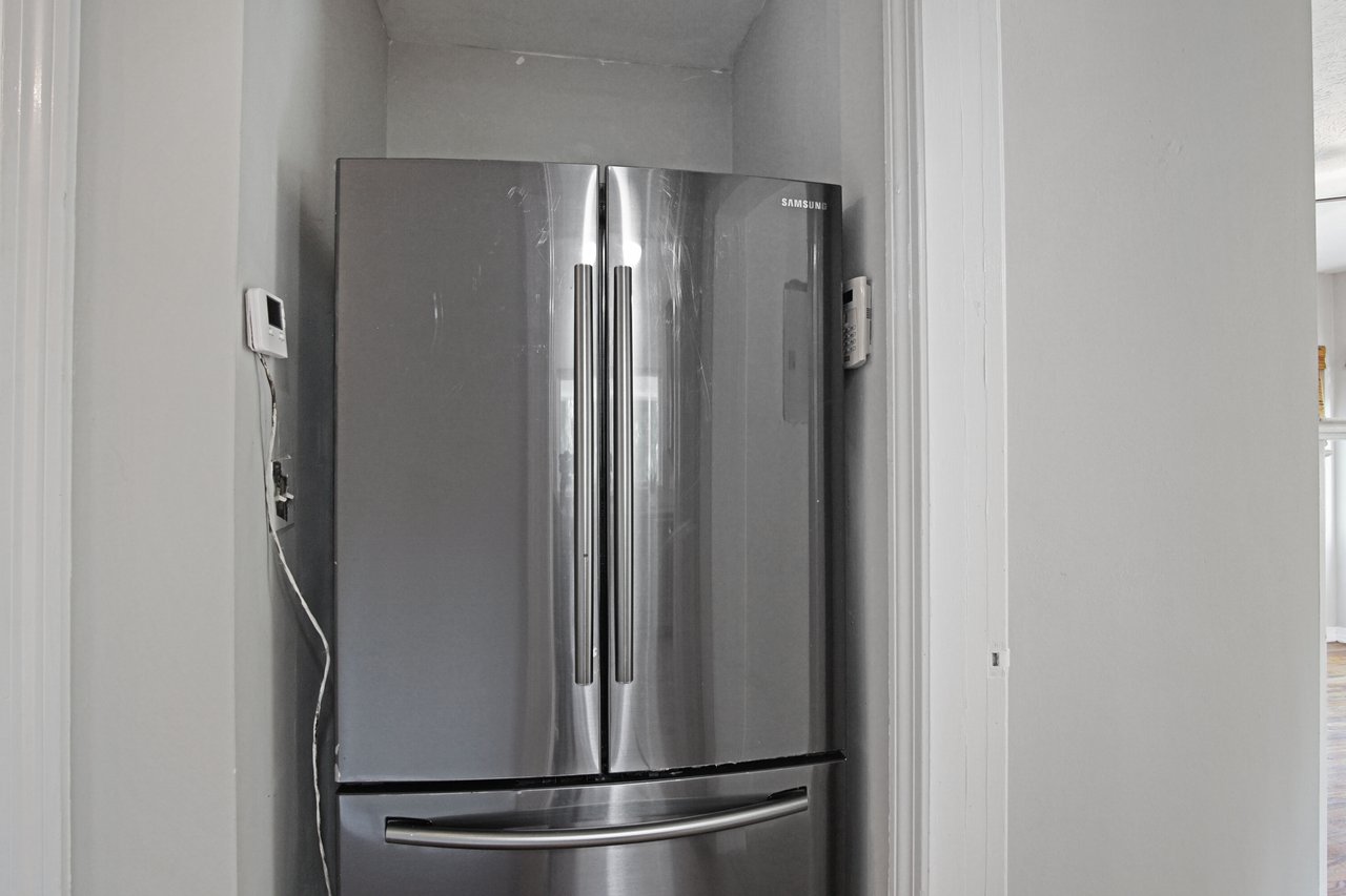 A sleek stainless steel refrigerator with French doors is snugly fitted in a narrow gray-walled alcove, exuding a modern and minimalistic ambiance.