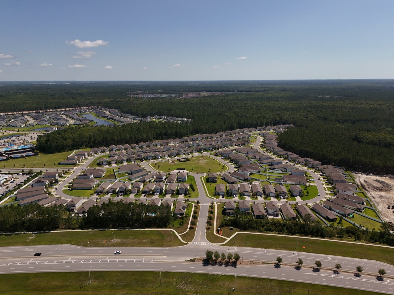 Aerial view of homes along curving streets, with a main road and dense woodland nearby.
