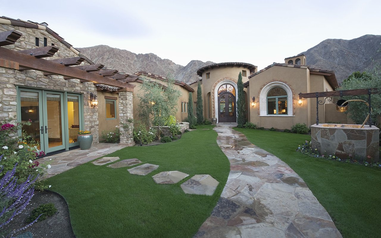 Mediterranean-style home with an arched entry, stone courtyard, and mountain backdrop.