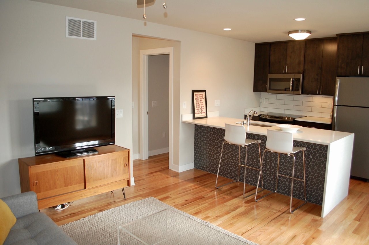 Furnished apartment kitchen and living area with a white peninsula, dark cabinets, and hardwood floors.