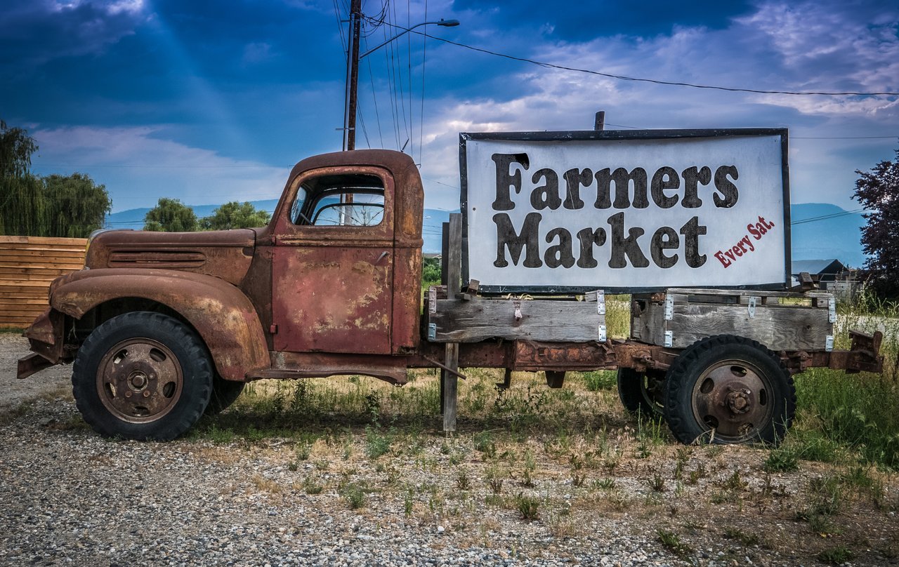Vintage pickup truck with a Farmers Market sign parked outside a Colorado farmers market with fresh produce and flowers