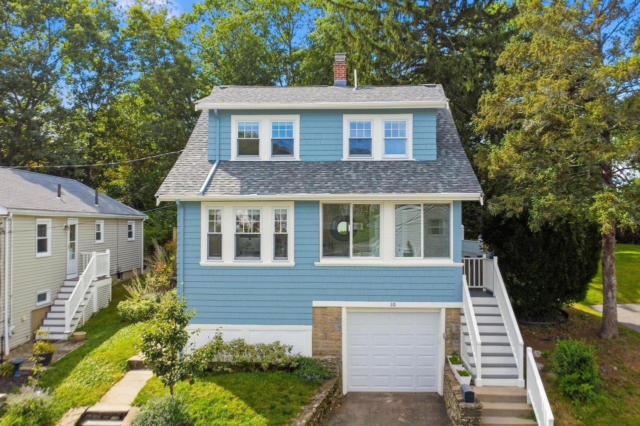 Blue two-story house with white trim, a gray shingle roof, and a front garage framed by leafy trees.