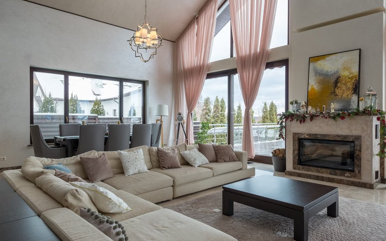 Living room with a cream sectional, stone fireplace, and tall windows with pink curtains.
