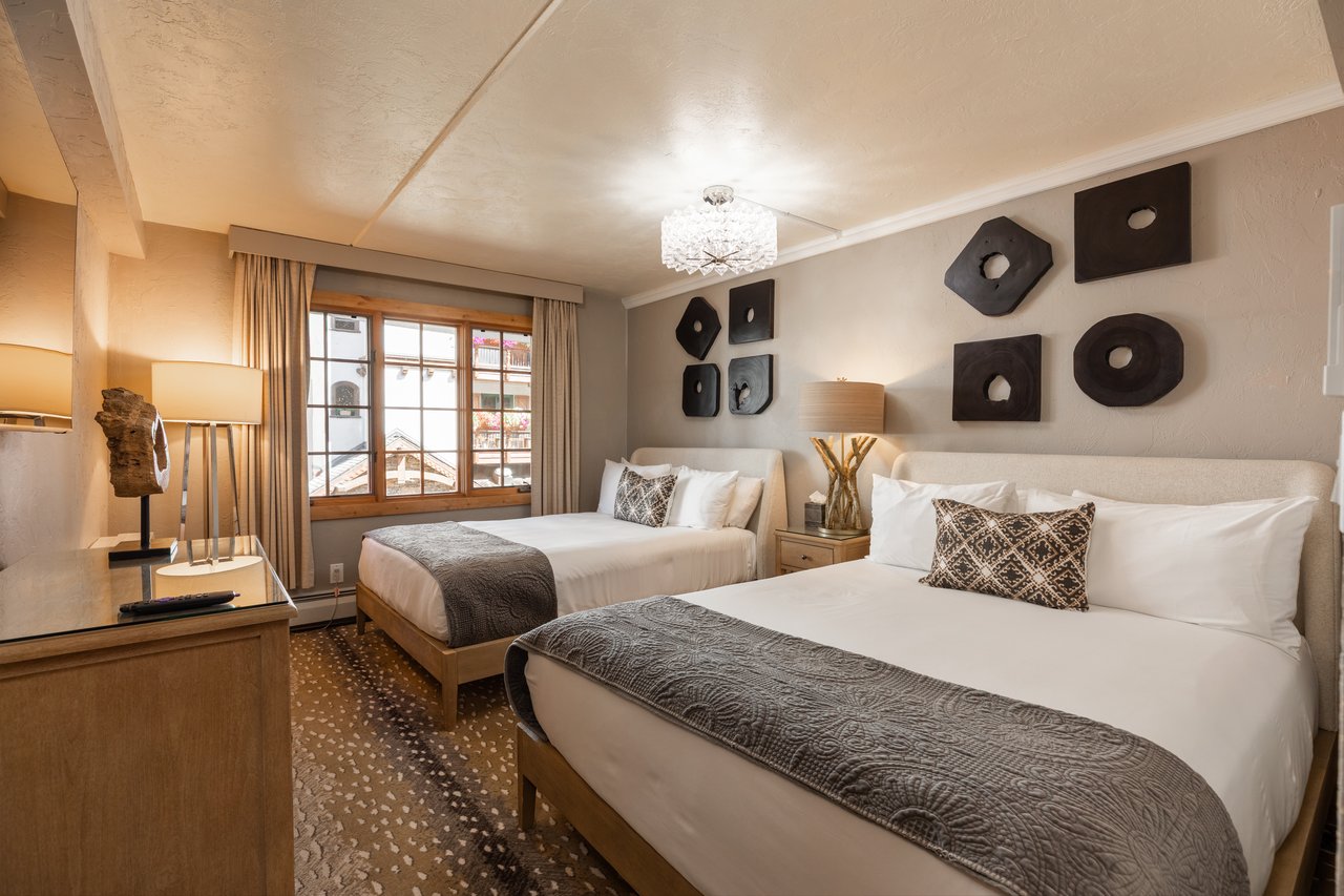 Bedroom with two queen beds, patterned gray runners, wood furnishings, and a large curtained window.