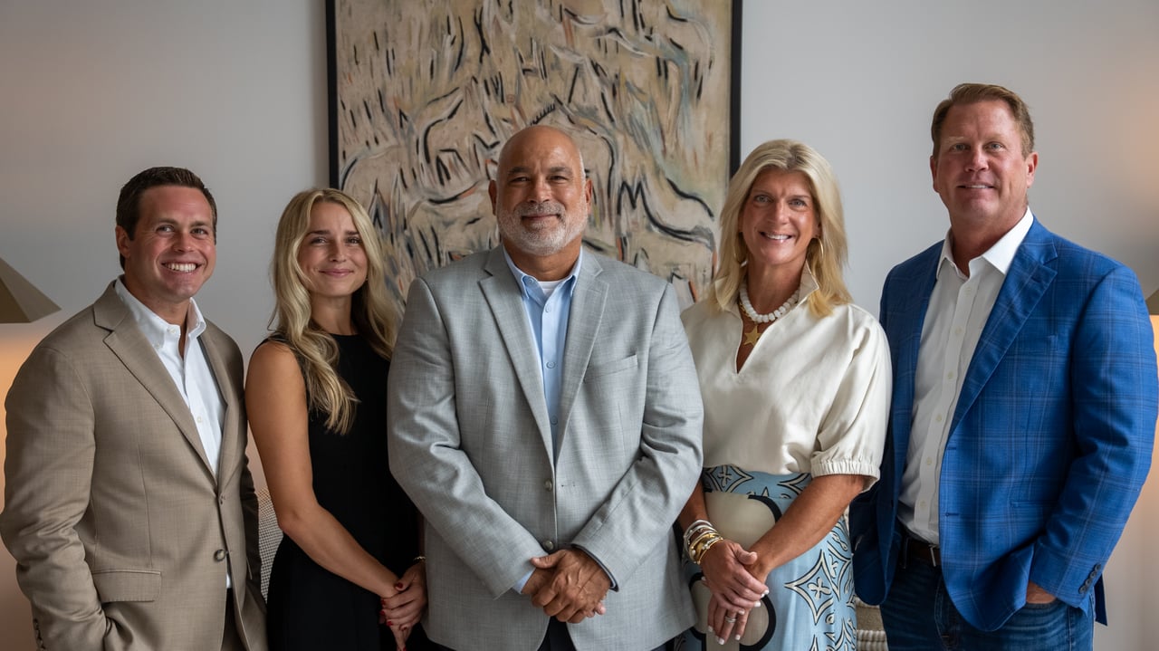 Five real estate agents pose together in business attire in front of an abstract painting.