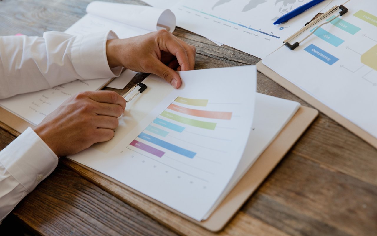 A person reviews colorful printed charts and reports on a rustic wooden table.