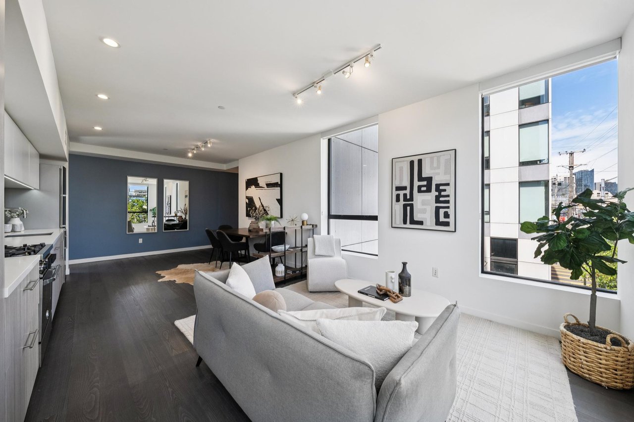 Open-plan condo living room with gray sofa, dining area, and large city-facing windows.
