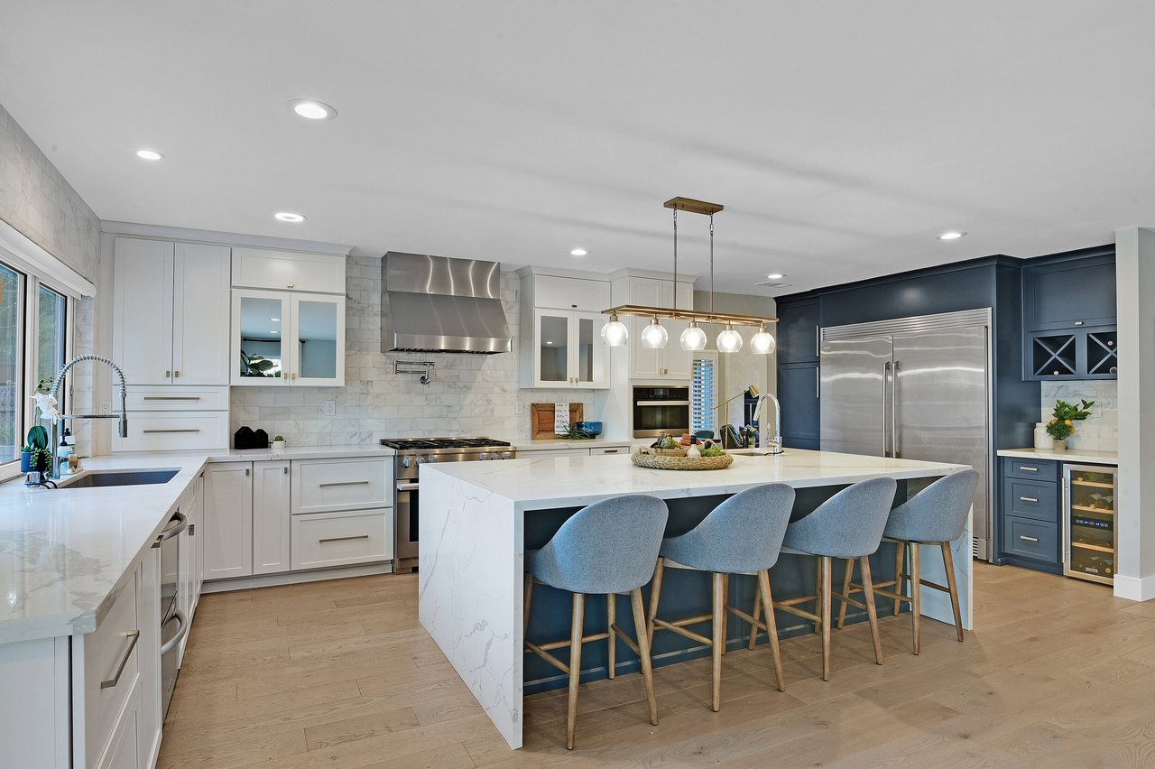 Modern kitchen with a large marble island, four stools, and dark navy cabinetry.