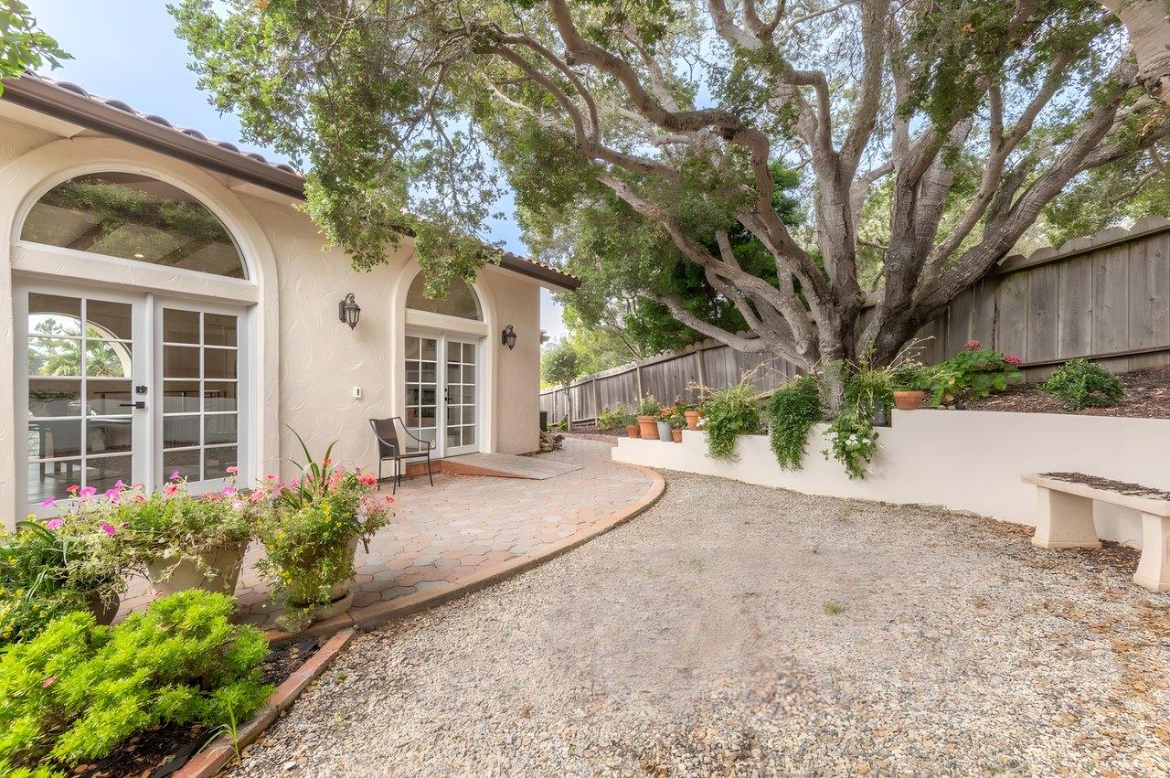 Home exterior with arched windows, a curved brick patio, and a large shade tree.