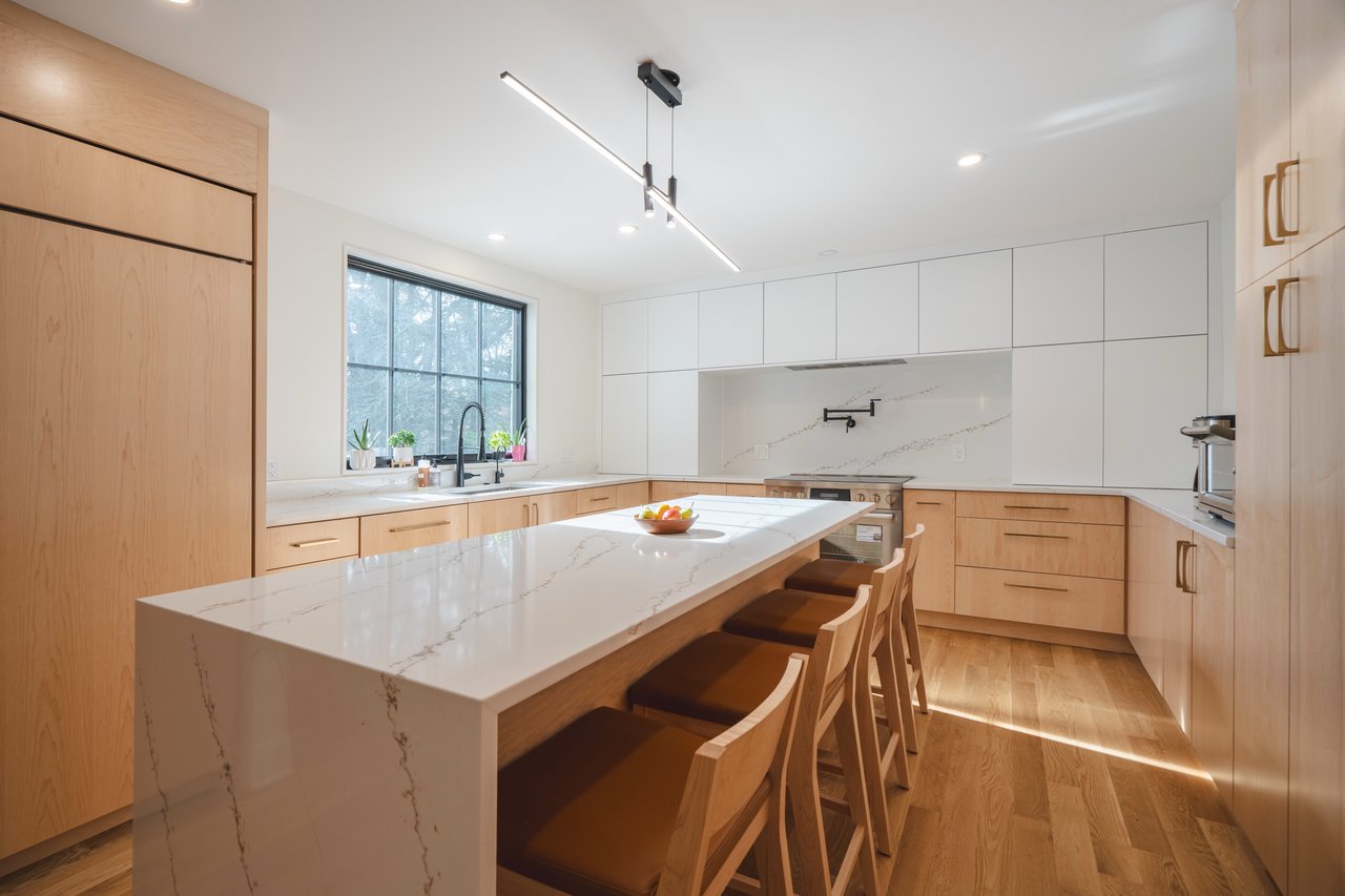 Modern kitchen with a marble-veined island, wood cabinetry, and black-framed window.