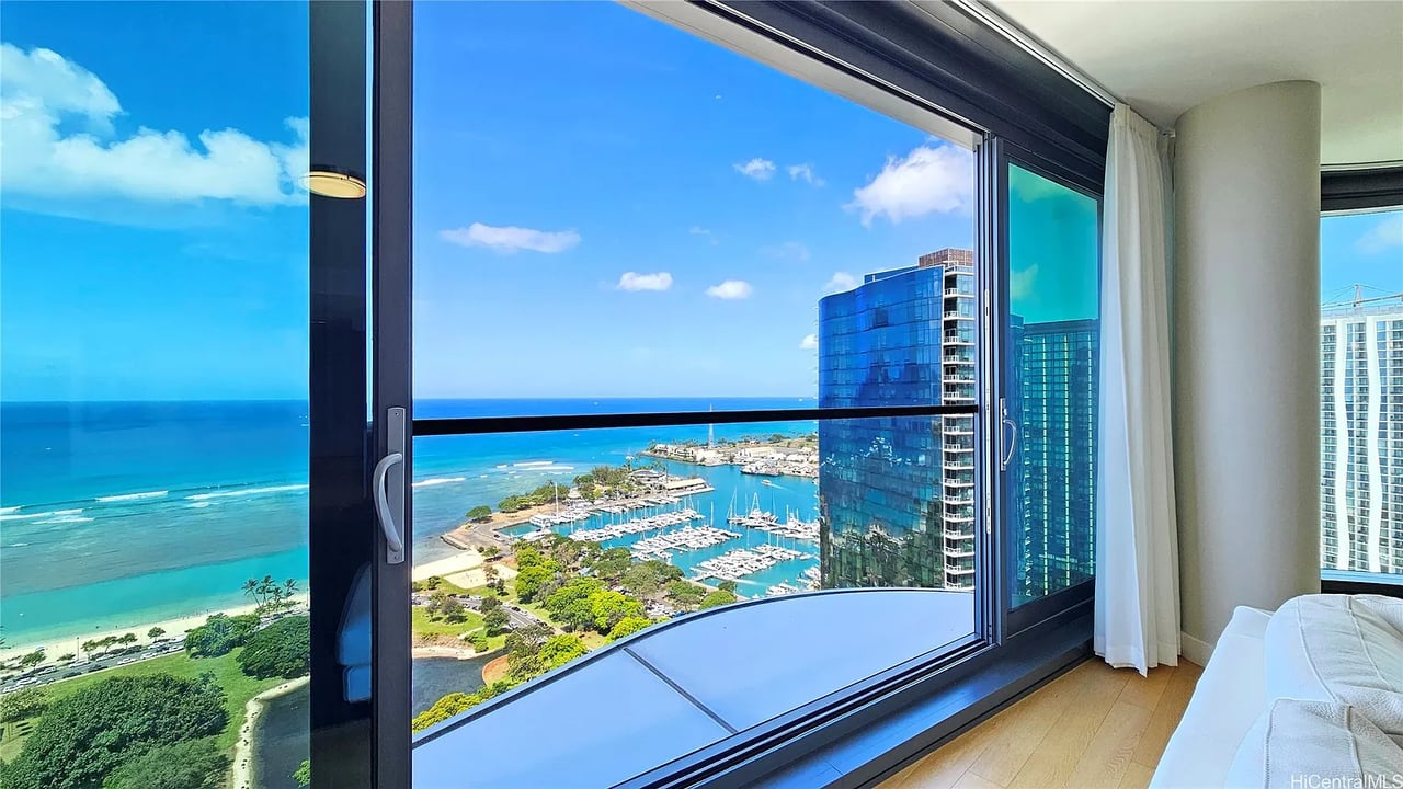 Condominium windows overlook the ocean and marina, with a blue-glass tower beside the harbor.