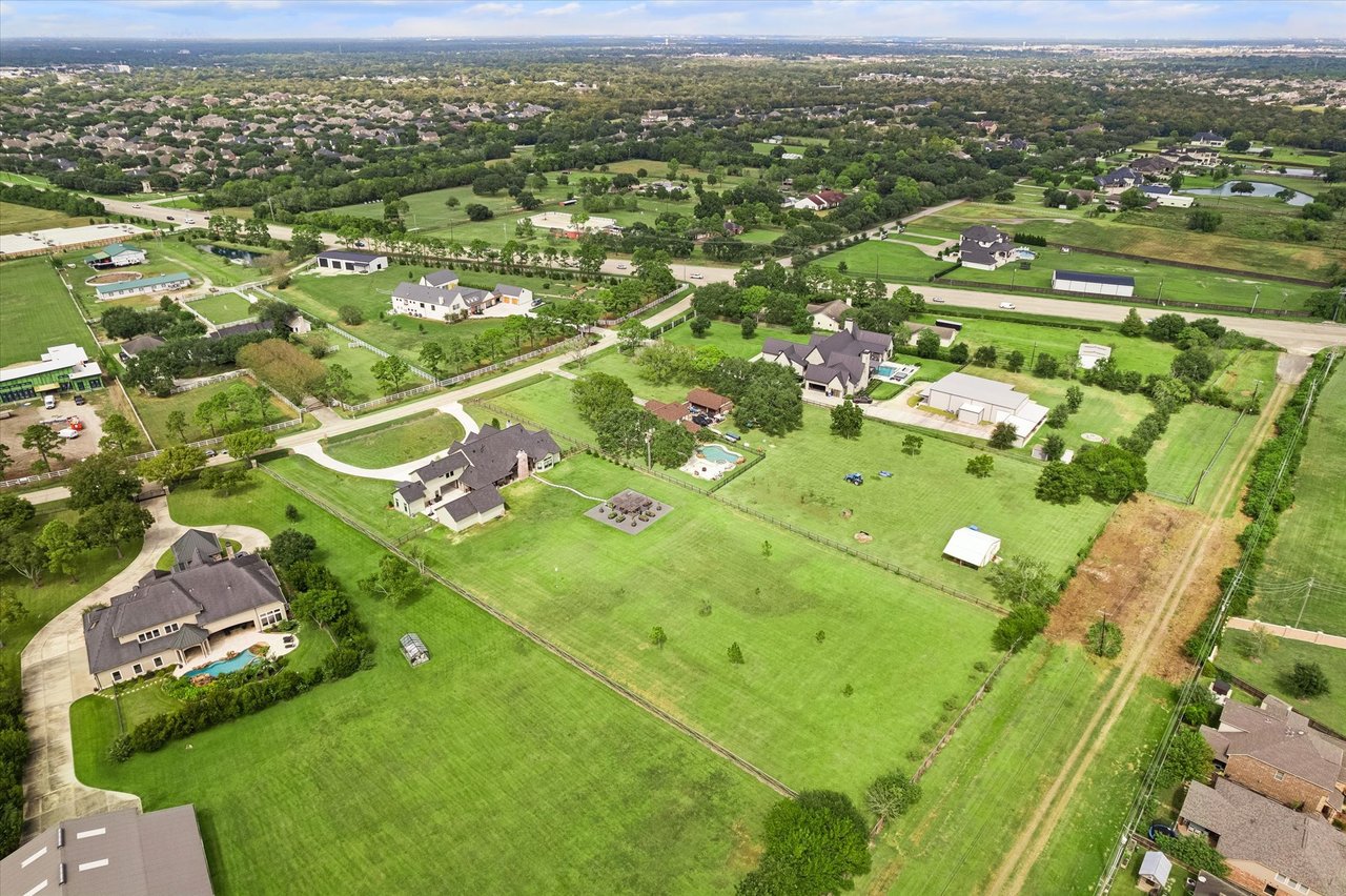 Aerial view of a large home and expansive green acreage among nearby homes.