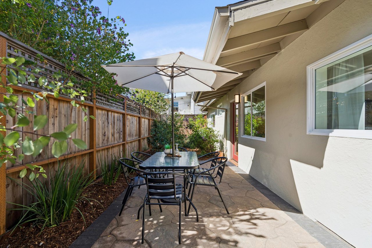 Fenced stone patio with an outdoor dining set beneath a large white umbrella.