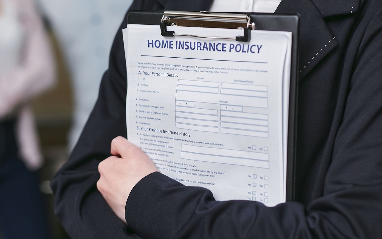 A clipboard with a home insurance policy form held by a person in a dark suit.