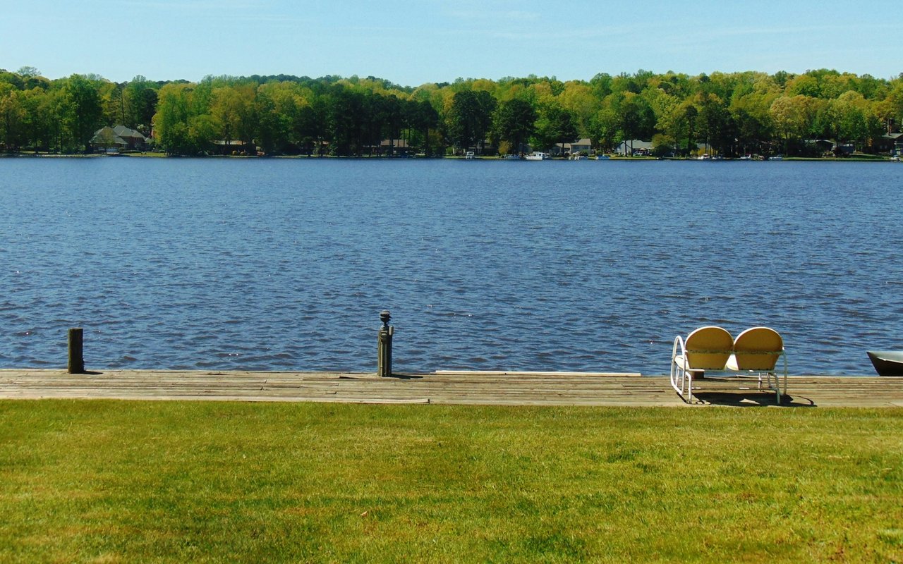 Lake shoreline with a wooden dock, grassy bank, and two yellow chairs.