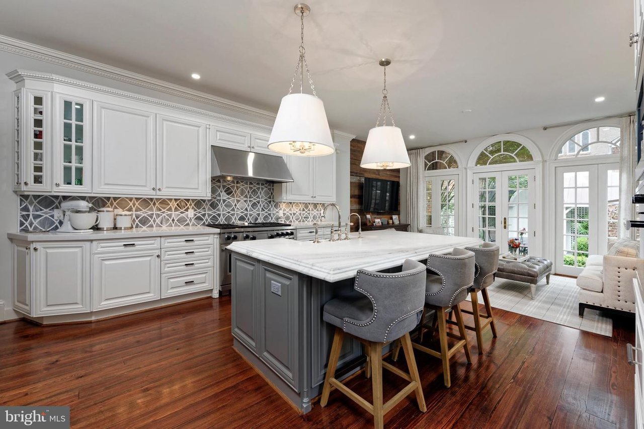 Kitchen with a large gray island, white cabinetry, patterned backsplash, and arched garden-facing windows.