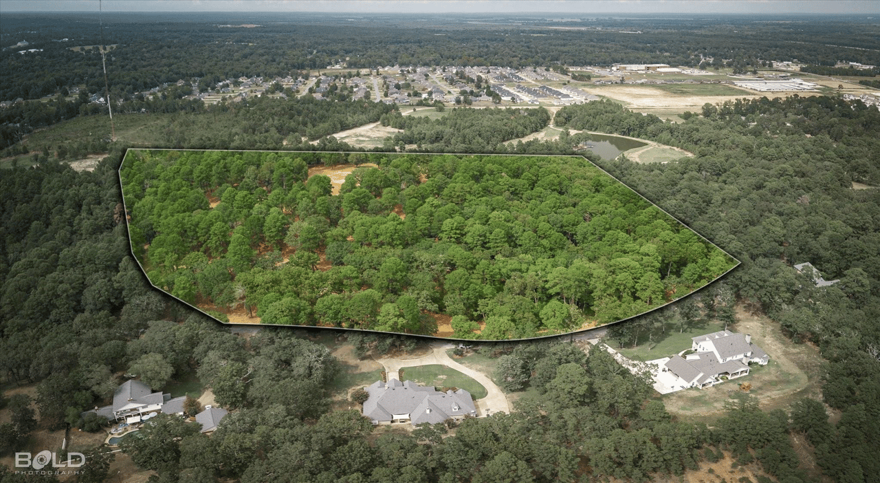 Aerial view of a wooded parcel outlined among nearby homes and development.