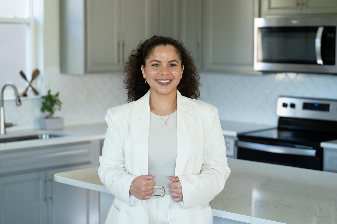 Kiara Morales Lopez in a white suit, standing in a bright modern kitchen.