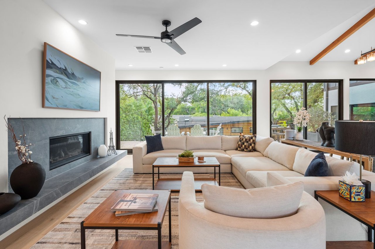 Living room with a cream sectional, stone fireplace, and wide windows overlooking trees.