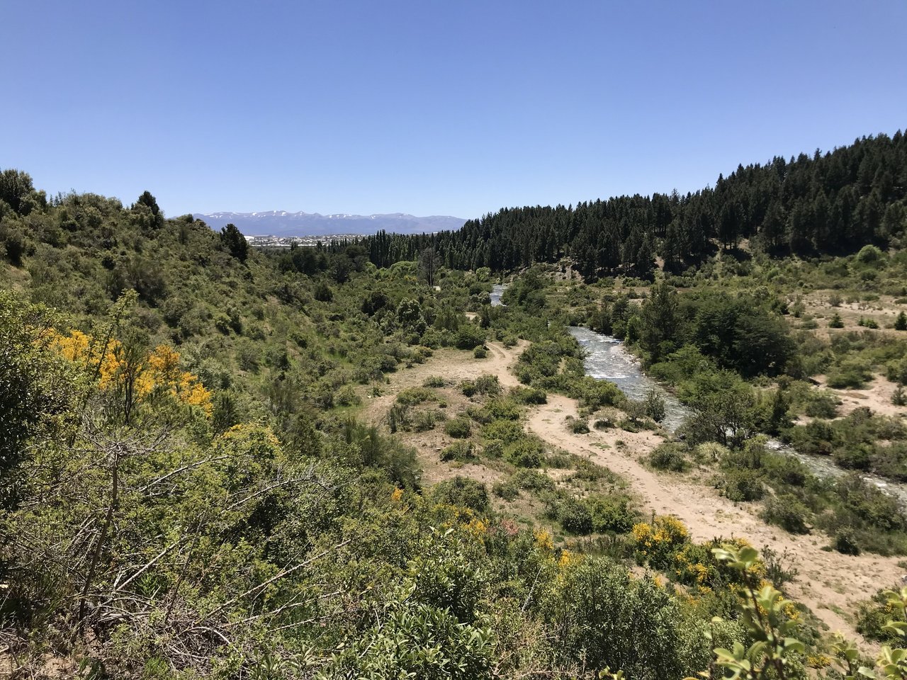 Rural land with a winding stream, forested hills, and distant mountains.