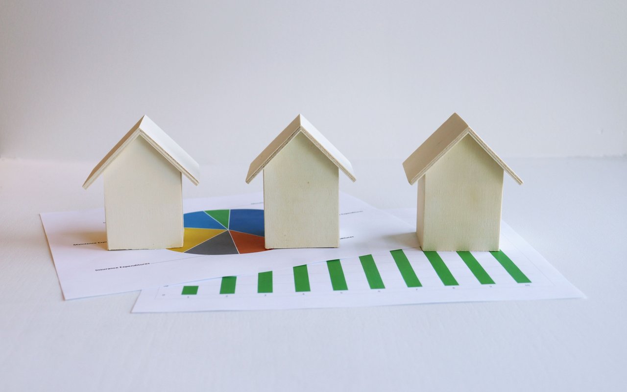 Three model houses arranged over real estate charts with green bars and a multicolored pie chart.