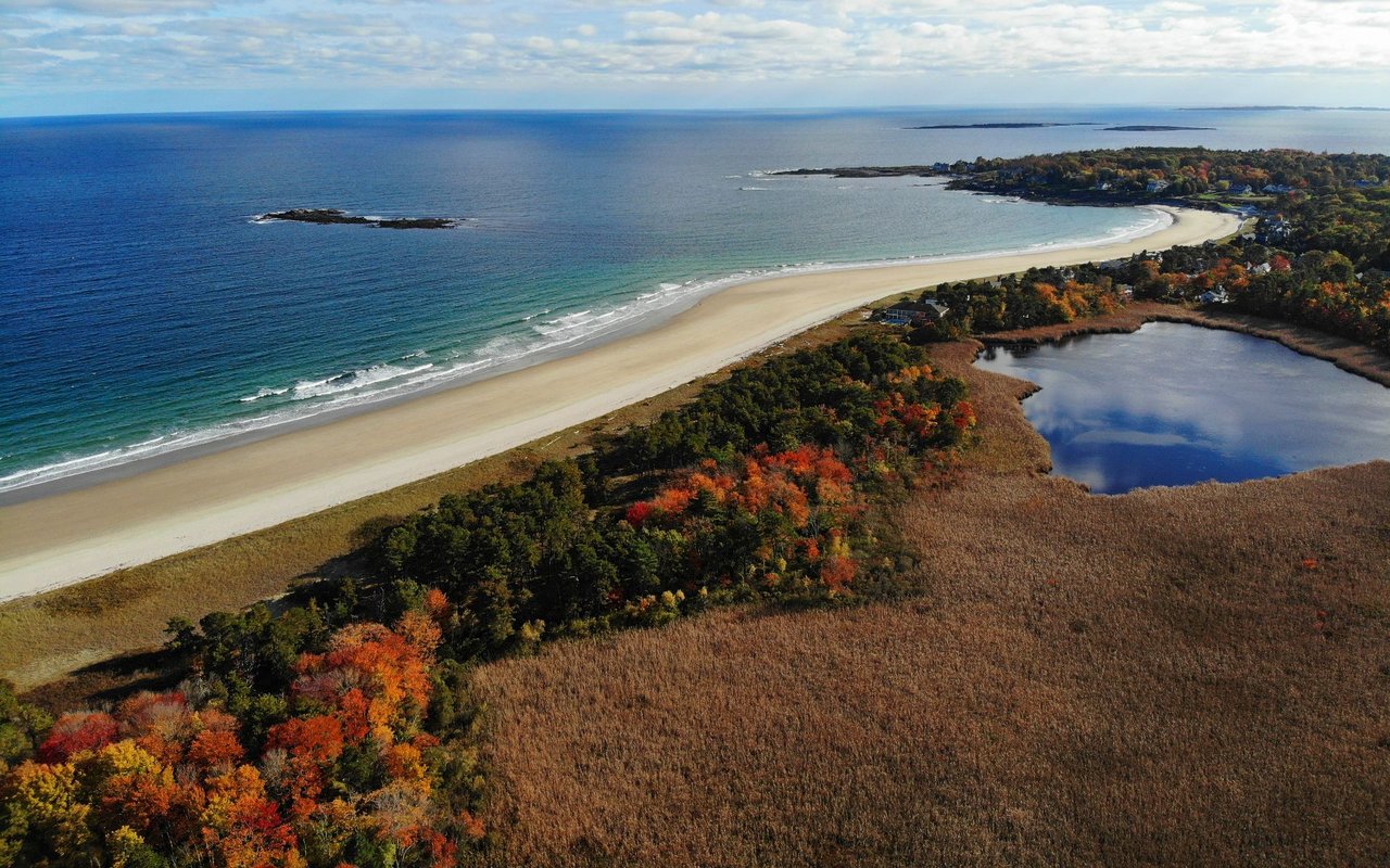Scarborough coastline with a curved sandy beach, ocean, salt marsh, and autumn foliage.