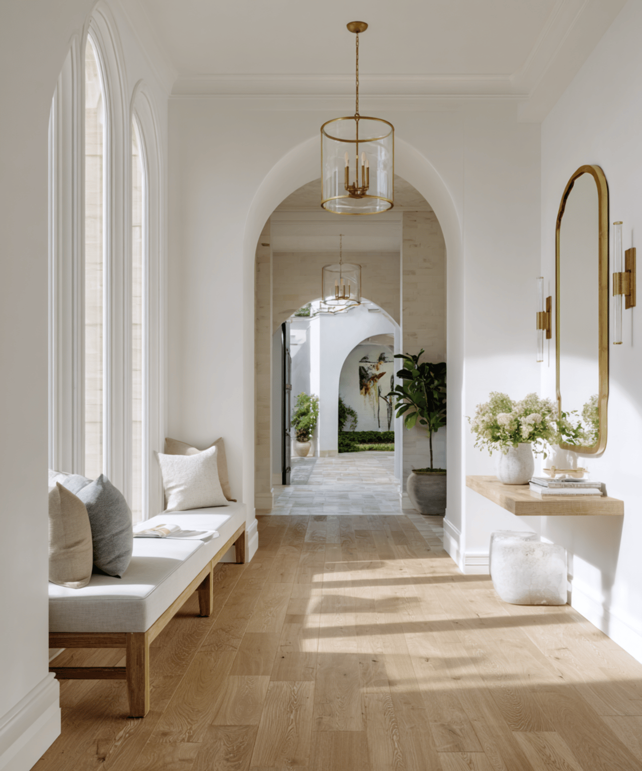 Bright entry hall with arched windows, oak floors, a built-in bench, and brass accents.