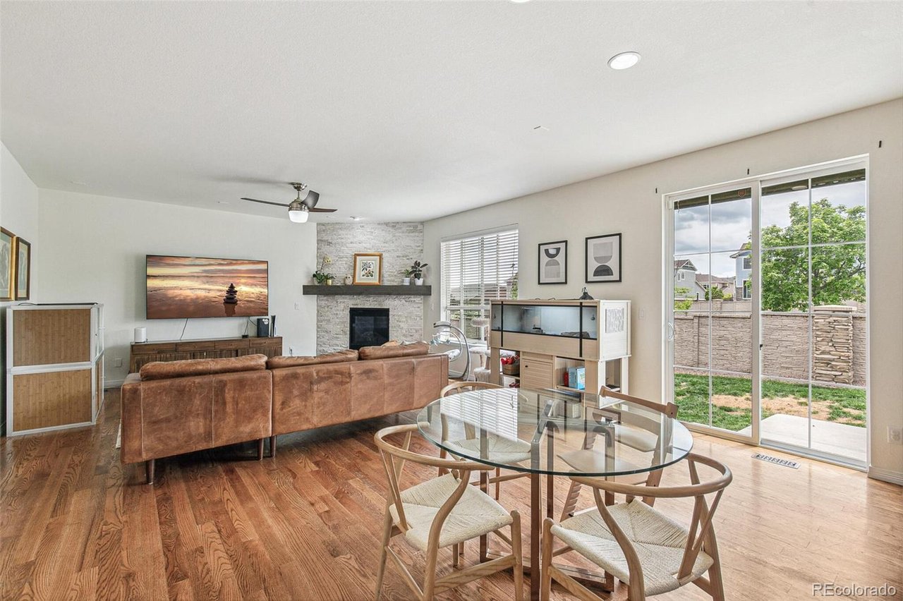 Open-plan living and dining room with a stone fireplace, leather sofa, and sliding doors to a fenced yard.