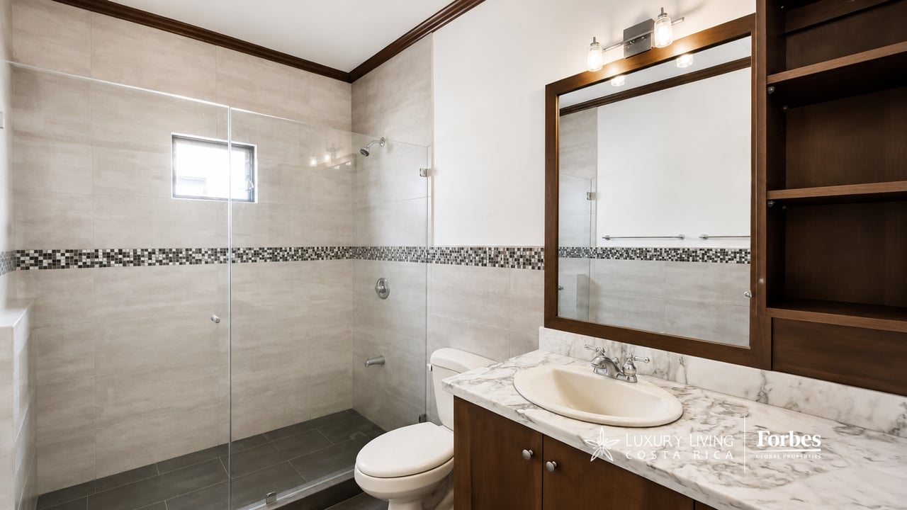 Bathroom with a glass shower, mosaic tile accent band, and dark wood vanity with marble countertop.