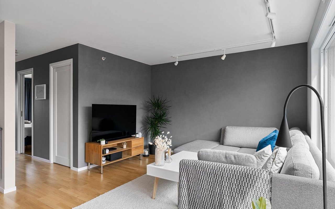 Living room with a gray sectional, dark walls, light wood floors, and large windows.