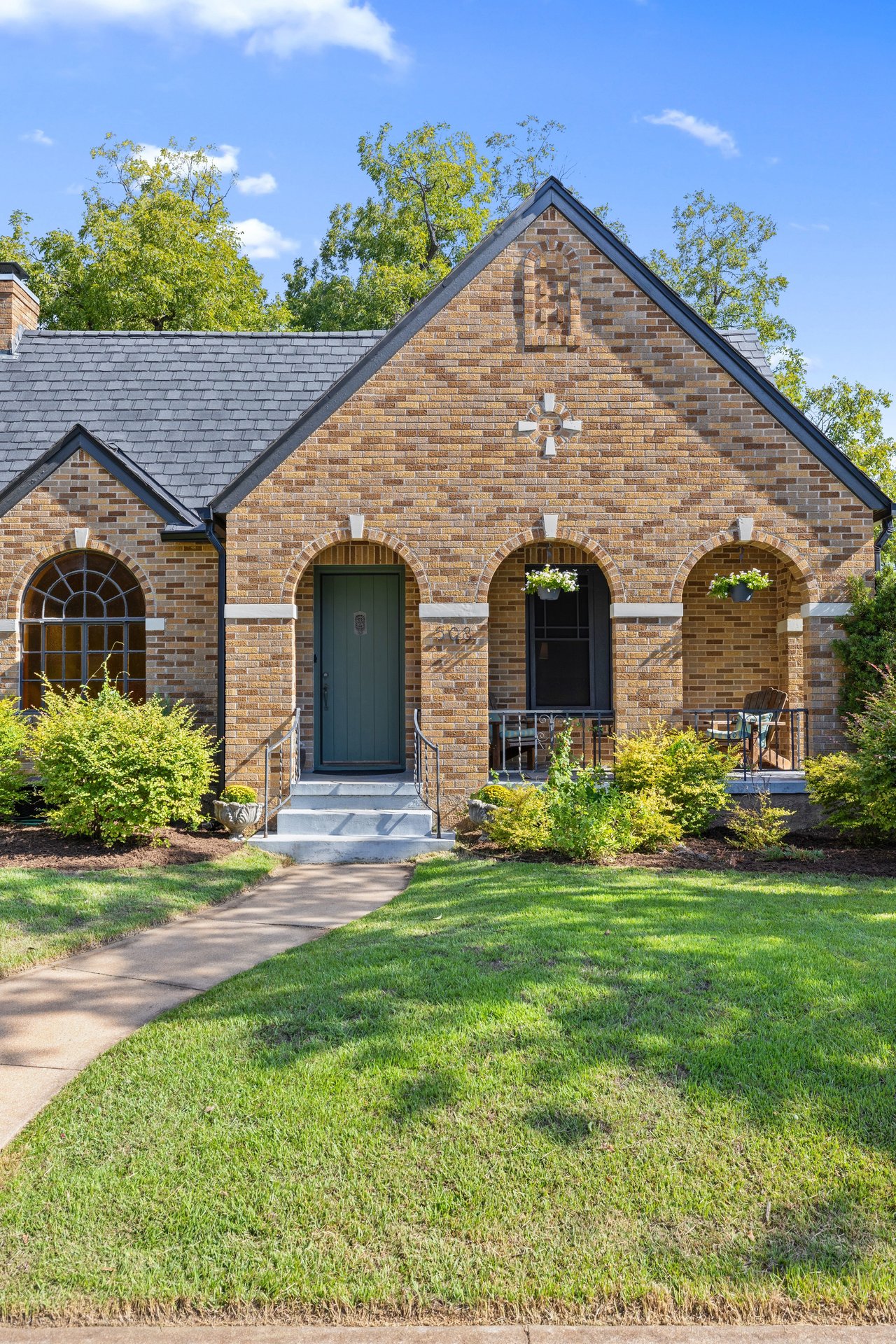 Brick house with a steep gabled roof, arched porch, dark green door, and curved walkway.